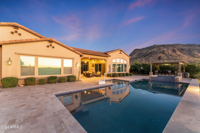 pool at dusk featuring an in ground hot tub, a mountain view, and a patio