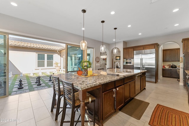 kitchen featuring light stone countertops, sink, hanging light fixtures, stainless steel appliances, and a kitchen island with sink