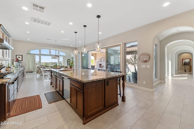 kitchen featuring light tile patterned floors, light stone countertops, decorative light fixtures, and a kitchen island with sink