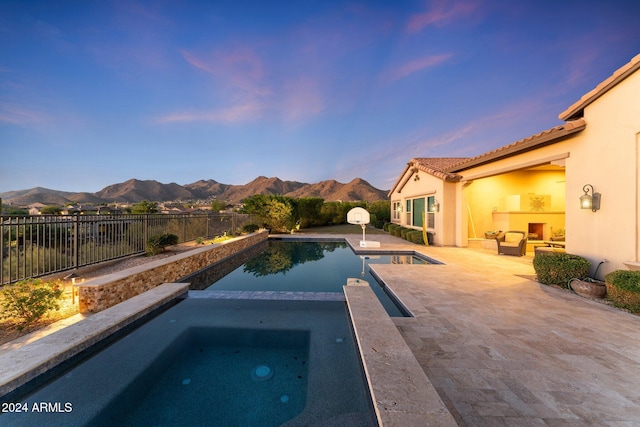 pool at dusk featuring an in ground hot tub, a mountain view, and a patio area