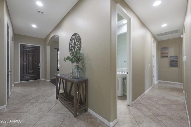 corridor featuring arched walkways, light tile patterned floors, visible vents, and baseboards