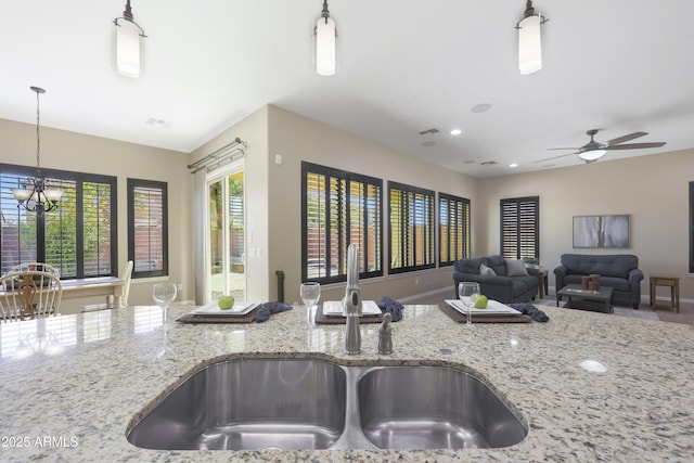 kitchen featuring visible vents, light stone counters, open floor plan, pendant lighting, and a sink