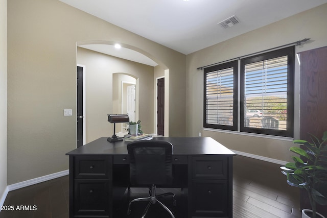 office space with arched walkways, visible vents, dark wood finished floors, and baseboards