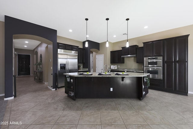 kitchen featuring arched walkways, appliances with stainless steel finishes, a large island, and dark cabinetry