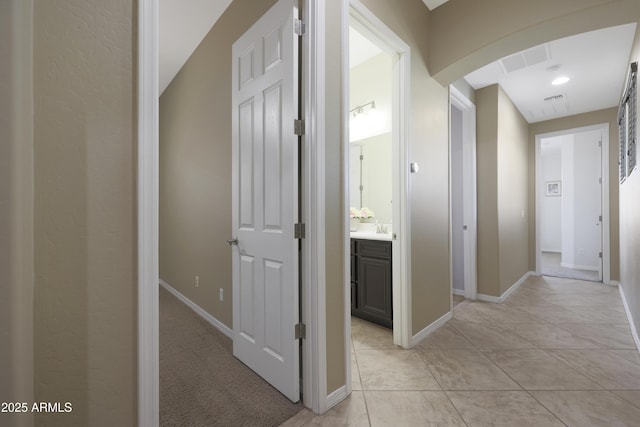 hallway featuring arched walkways, light tile patterned floors, visible vents, a sink, and baseboards