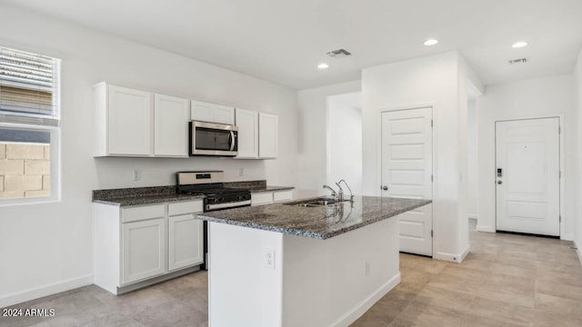 kitchen with stove, white cabinets, dark stone countertops, sink, and a center island with sink