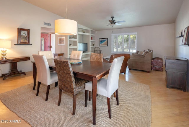 dining area featuring ceiling fan, built in shelves, light hardwood / wood-style flooring, and vaulted ceiling