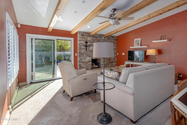 carpeted living room with ceiling fan, vaulted ceiling with beams, and a stone fireplace