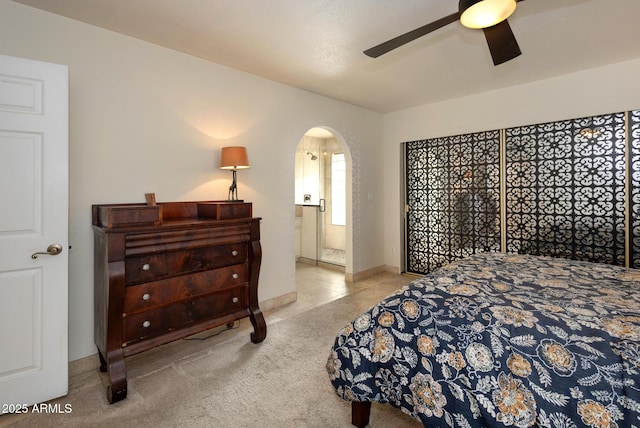 bedroom featuring ceiling fan, light colored carpet, and ensuite bath