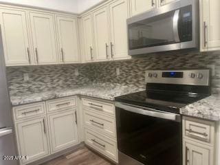 kitchen with hardwood / wood-style floors, cream cabinets, tasteful backsplash, light stone counters, and stainless steel appliances