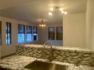 kitchen featuring light stone counters, a notable chandelier, and sink