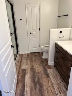 bathroom featuring toilet, a stall shower, wood finished floors, and vanity