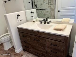 bathroom featuring toilet, walk in shower, wood finished floors, and vanity