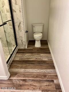 bathroom with wood-type flooring, a shower with shower door, and toilet