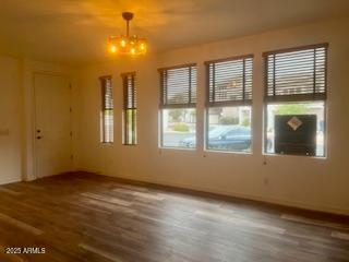 spare room with wood finished floors, a wealth of natural light, and a notable chandelier