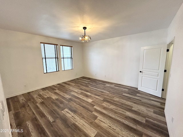 unfurnished room with dark wood-style floors, baseboards, and an inviting chandelier