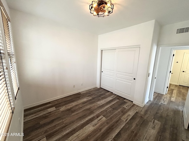 unfurnished bedroom with visible vents, baseboards, dark wood finished floors, and a closet