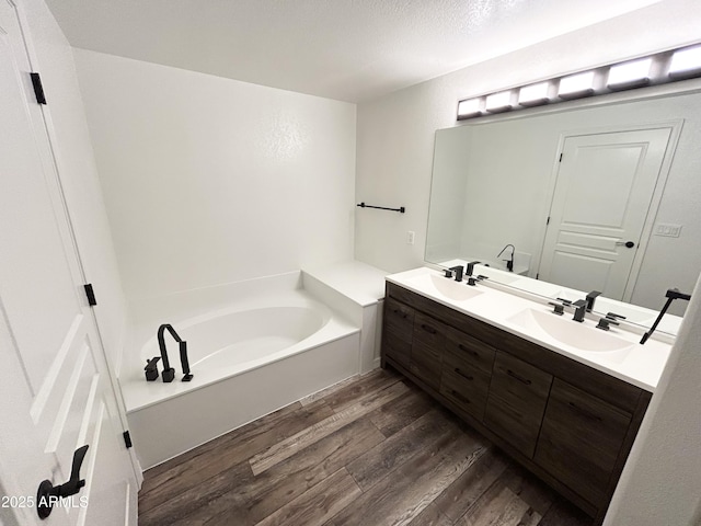 full bath with a garden tub, double vanity, wood finished floors, and a sink