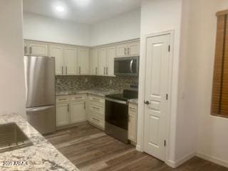 kitchen featuring light stone counters, dark wood-style flooring, backsplash, appliances with stainless steel finishes, and baseboards