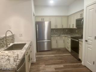 kitchen with light stone counters, stainless steel appliances, dark wood-type flooring, a sink, and backsplash