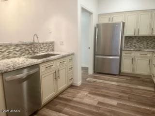 kitchen with dark wood-type flooring, a sink, appliances with stainless steel finishes, decorative backsplash, and light stone countertops