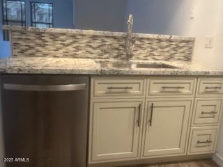 kitchen featuring light stone counters, cream cabinets, a sink, and stainless steel dishwasher