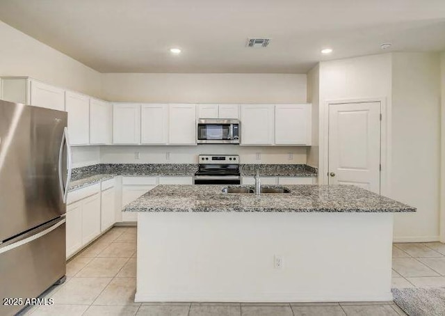 kitchen featuring light stone countertops, appliances with stainless steel finishes, a kitchen island with sink, and white cabinets