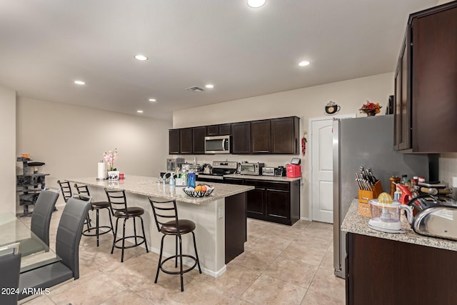 kitchen featuring appliances with stainless steel finishes, a kitchen breakfast bar, light stone counters, dark brown cabinets, and light tile patterned floors