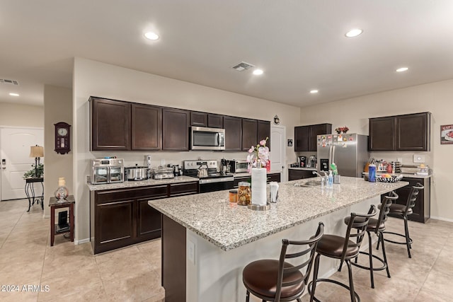 kitchen featuring a breakfast bar, a center island with sink, stainless steel appliances, and dark brown cabinets