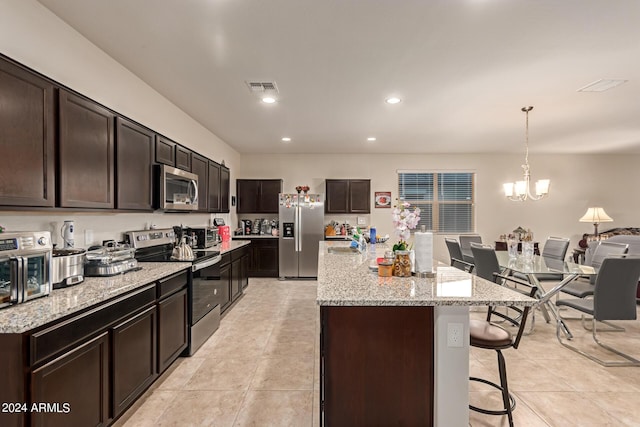 kitchen with pendant lighting, light tile patterned floors, an island with sink, a notable chandelier, and stainless steel appliances