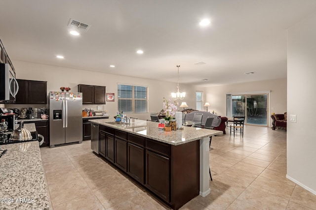 kitchen with dark brown cabinetry, stainless steel appliances, a kitchen island with sink, sink, and decorative light fixtures