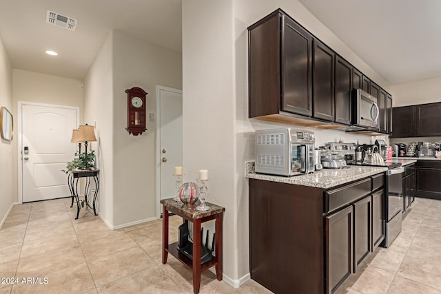 kitchen featuring dark brown cabinetry, light stone countertops, light tile patterned floors, and appliances with stainless steel finishes