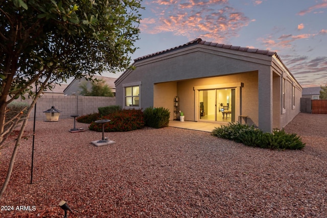 back house at dusk featuring a patio