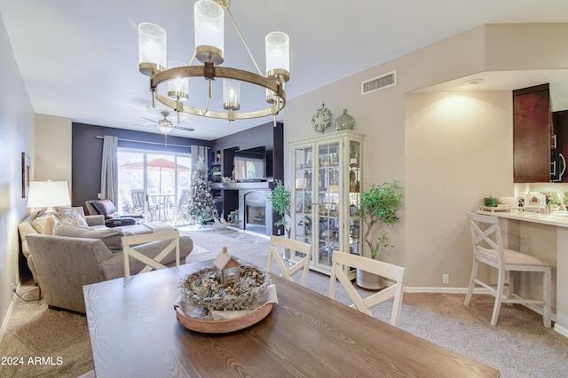 carpeted dining room featuring ceiling fan with notable chandelier and a fireplace