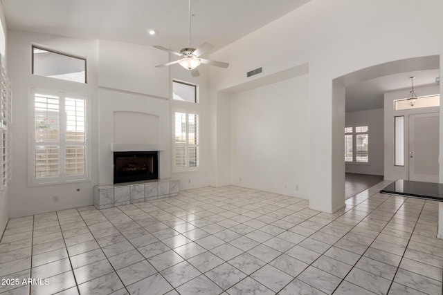 unfurnished living room featuring a fireplace with raised hearth, arched walkways, marble finish floor, a ceiling fan, and visible vents