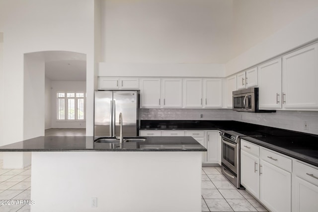 kitchen with a sink, arched walkways, white cabinets, and stainless steel appliances