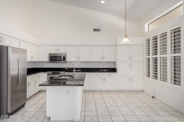kitchen with dark countertops, a sink, stainless steel appliances, white cabinetry, and pendant lighting