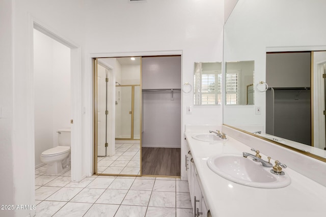full bathroom with toilet, a walk in closet, a sink, and marble finish floor