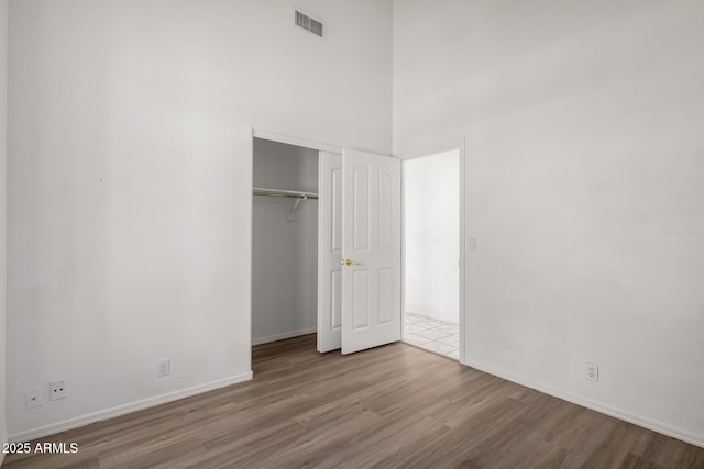 unfurnished bedroom featuring visible vents, wood finished floors, baseboards, a closet, and a high ceiling