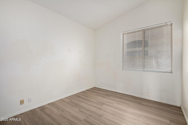 unfurnished room with baseboards, vaulted ceiling, and light wood finished floors