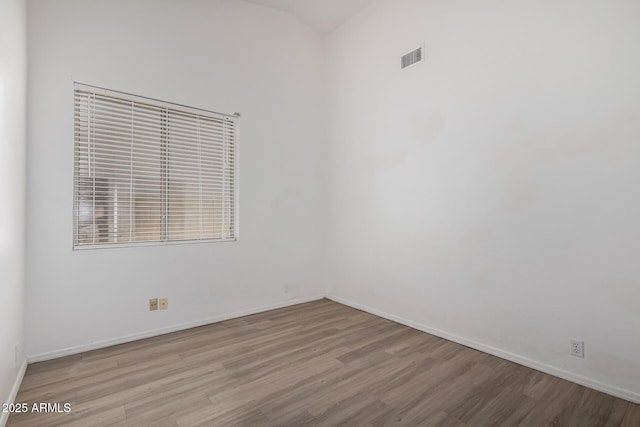 empty room featuring baseboards, visible vents, wood finished floors, and lofted ceiling