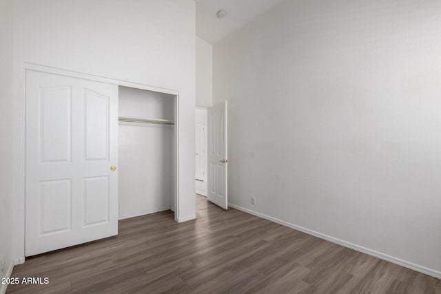 unfurnished bedroom featuring baseboards, wood finished floors, high vaulted ceiling, and a closet