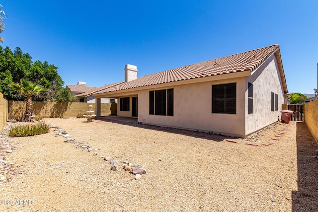rear view of house featuring a fenced backyard, a chimney, stucco siding, and a tile roof