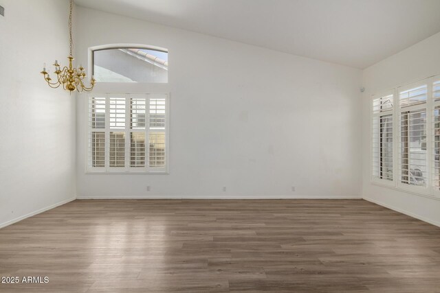 empty room featuring plenty of natural light, wood finished floors, vaulted ceiling, and an inviting chandelier