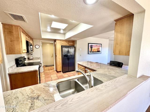 kitchen featuring a textured ceiling, light tile patterned floors, black appliances, a skylight, and sink