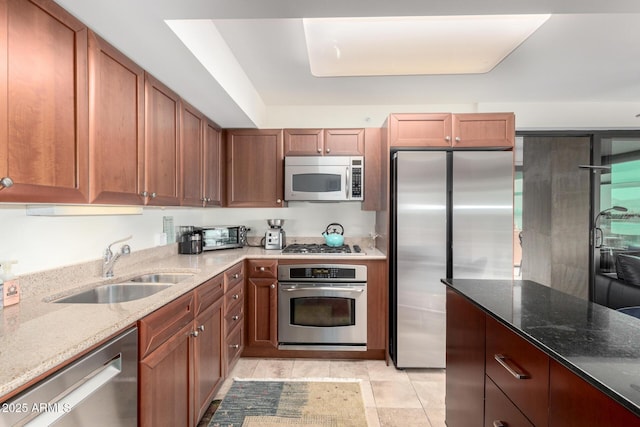 kitchen with stainless steel appliances, brown cabinets, a sink, and light stone counters