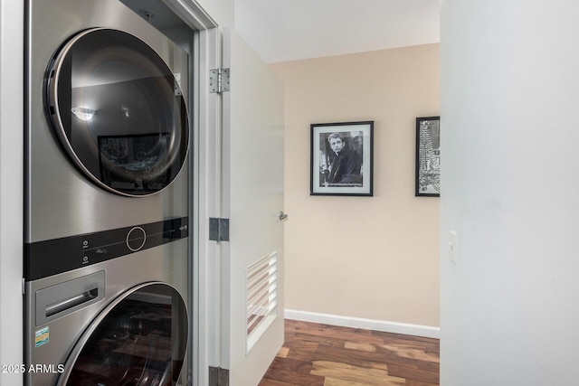 washroom featuring laundry area, stacked washing maching and dryer, wood finished floors, and baseboards