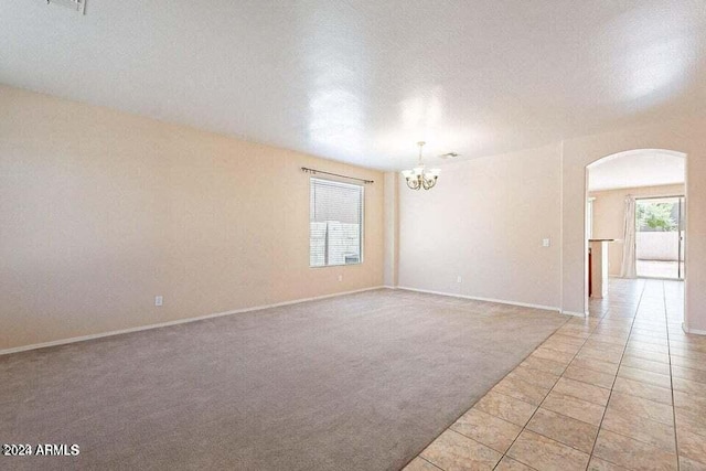 spare room featuring light carpet, a textured ceiling, and an inviting chandelier