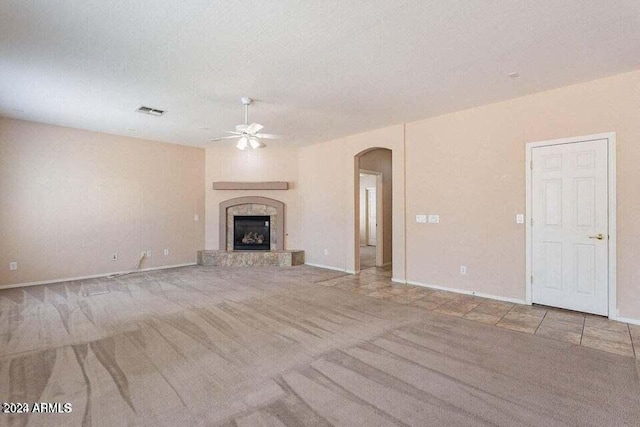 unfurnished living room with a tile fireplace, a textured ceiling, light colored carpet, and ceiling fan