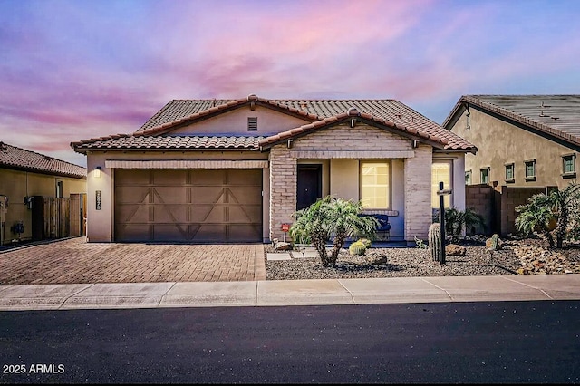 view of front of house featuring fence, an attached garage, stucco siding, a tile roof, and decorative driveway